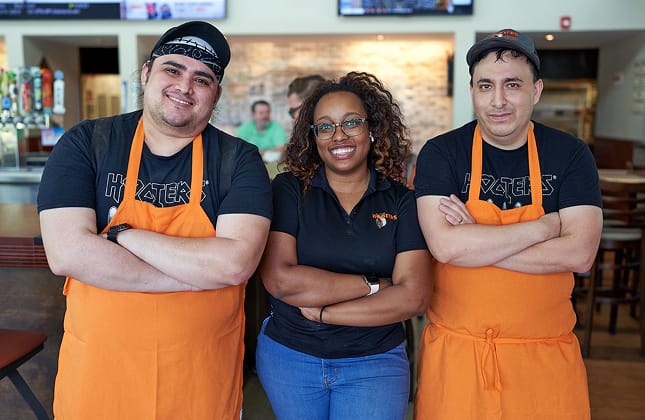 A photo of a restaurant manager and two employees at a Hooters restaurant